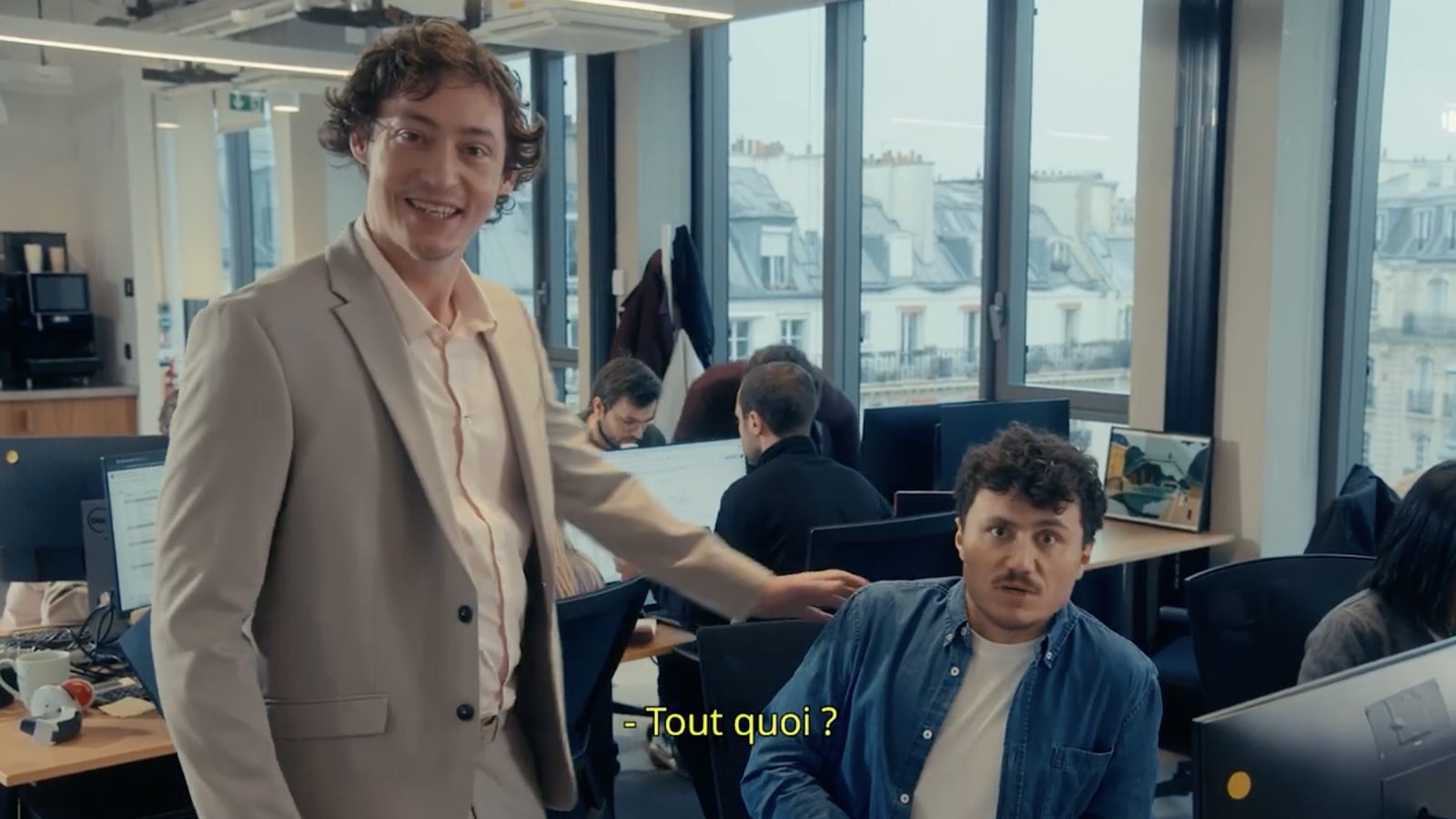 Le Coach pose la main sur l'épaule d'un salarié dans un open space. Sous-titre : Tout quoi ?