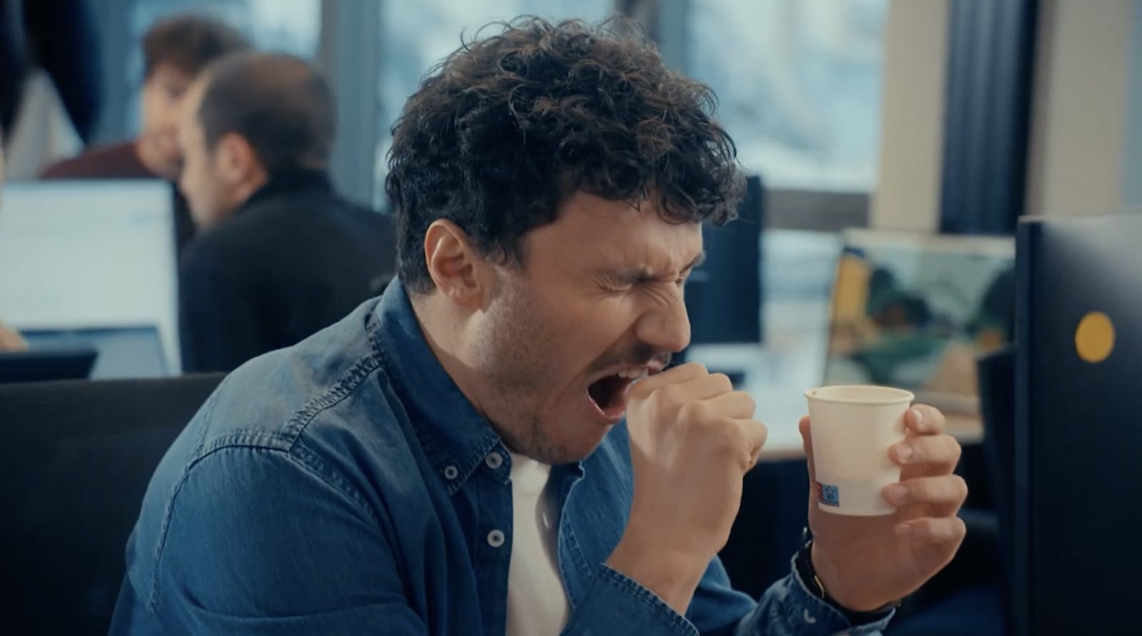 Un salarié grimace en buvant un café dans un gobelet.
